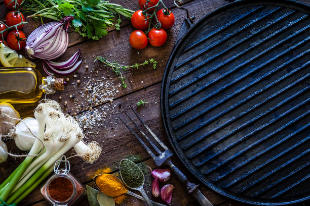 Empty griddle and ingredients for cooking Empty old iron griddle with ingredients for cooking shot from above on rustic wooden kitchen table. Ingredients and spices included in the composition are lemon, garlic, onion, tomatoes, parsley, bay leaf, chive, olive oil, salt, pepper and others. Cooking background. Low key DSRL studio photo taken with Canon EOS 5D Mk II and Canon EF 100mm f/2.8L Macro IS USM griddle stock pictures, royalty-free photos & images