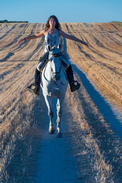 A woman enjoying horseback riding on a scenic trail, surrounded by nature and tranquility, in a picturesque countryside setting. The warm golden hour light enhances the peaceful atmosphere.