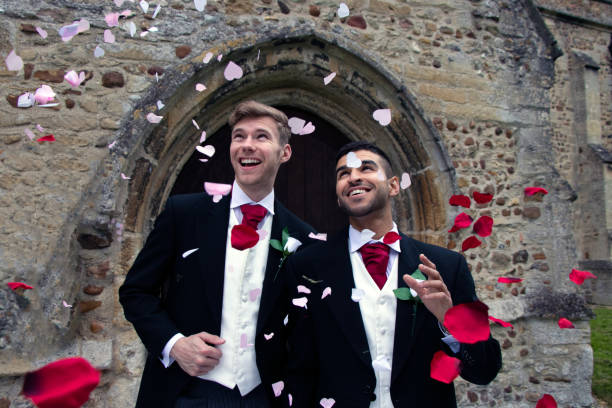 gay wedding, grooms leave village church after being married to smiles and confetti - sex sexual activity sexual issues couple imagens e fotografias de stock