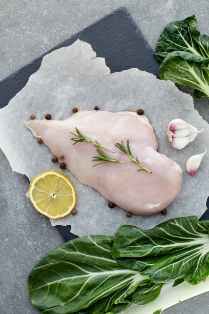 raw chicken breast with spices, garlic, lemon and green salad leafs on a grey stone table. top view. - garlic chicken breast raw chicken imagens e fotografias de stock