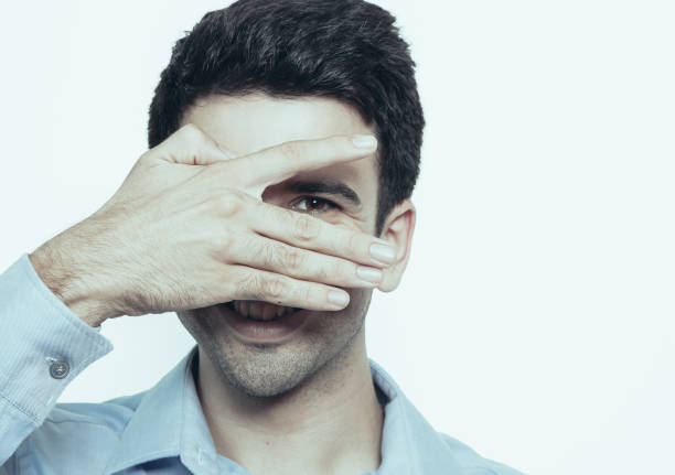 istock Cheerful young man peeking through fingers and looking at camera. Playful guy hiding face behind hand. Positive emotion concept 959243808