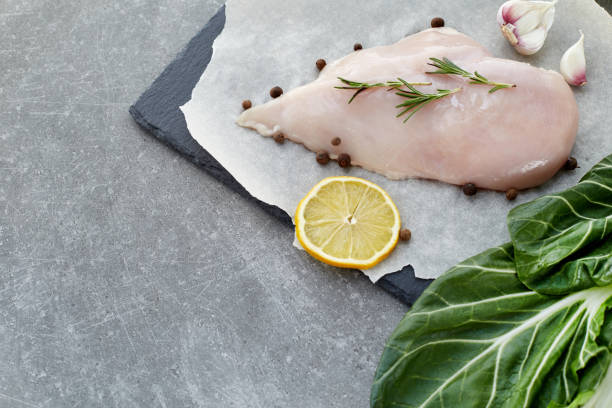 raw chicken breast with spices, garlic, lemon and green salad leafs on a grey stone table. - garlic chicken breast raw chicken imagens e fotografias de stock