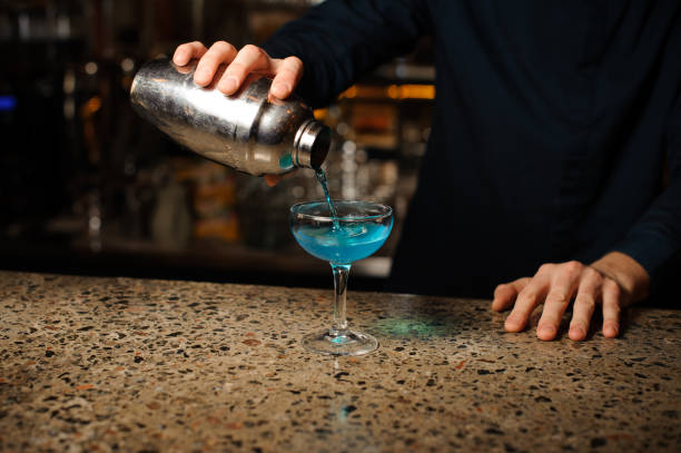 istock Barman hand pouring fresh drink with blue liquor from a shaker into a glass using strainer 959252324