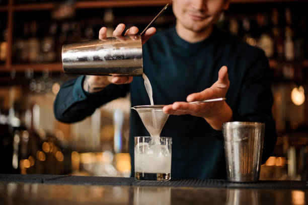 istock Smiling bartender pouring fresh drink from a shaker into a glass using strainer 959252750