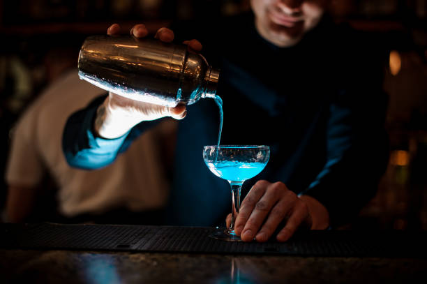 smiling barman pouring fresh drink with blue liquor from a shaker into a glass using strainer - men elegance cocktail cool imagens e fotografias de stock