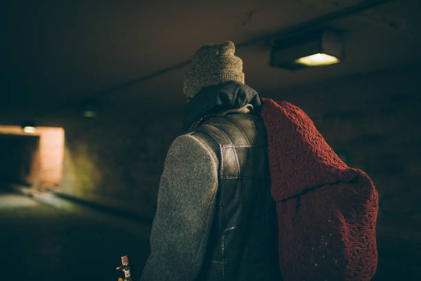 One man, young homeless man holding acoustic guitar, walking away, rear view.