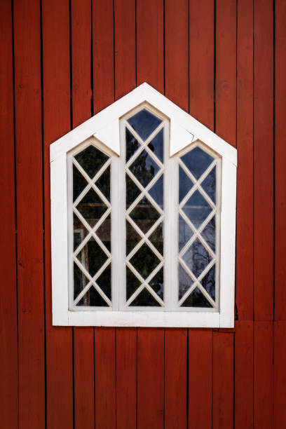 One white decorative traditional window with wooden frame on a red barn wall. Vertical composition.