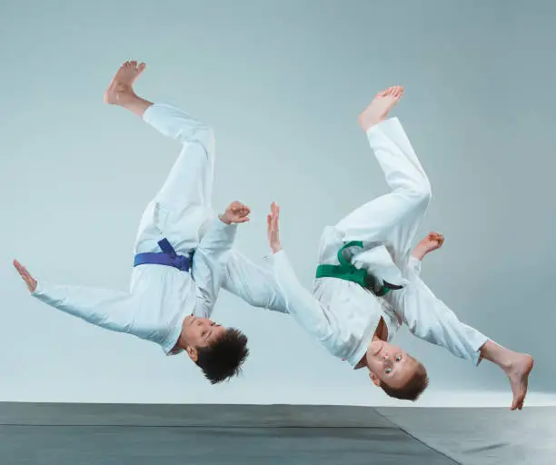 The teen boys fighting at Aikido training in martial arts school. Healthy lifestyle and sports concept. Teenagers in white kimono on white background. Children with concentrated faces