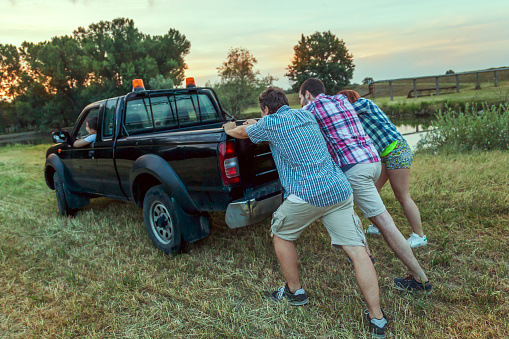 group of friends pushing the broken car on a country road