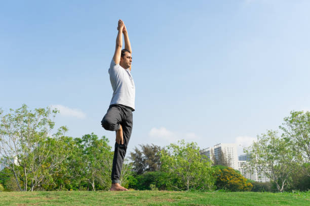 istock Indian male yoga instructor standing in tree pose on green lawn 959287126