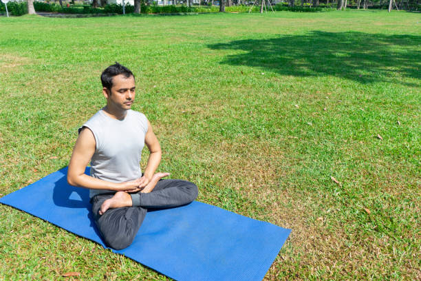 istock Indian man meditating in lotus pose on mat on grass 959287760