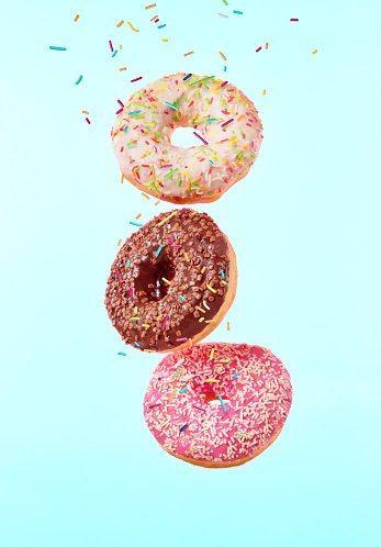 Flying sweet donuts isolated on light blue background. Concept of low gravity food in freeze motion effect. High resolution image