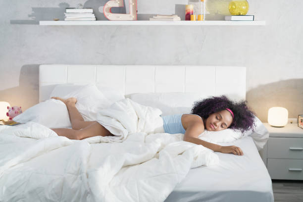 Black Woman Sleeping Alone in Large Bed Young African American woman waking up at home. Portrait of happy black girl smiling, enjoying a large king size mattress all for herself. waking up photos stock pictures, royalty-free photos & images