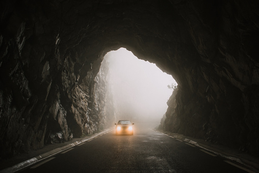A car with lights on, entering a tunnel road