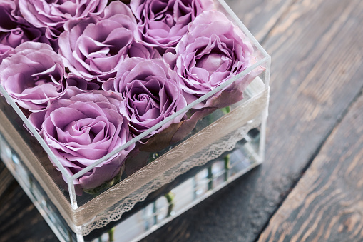 Pastel purple hue roses in clear acrylic crystal flower box. Square glass gift box. On wooden table from above