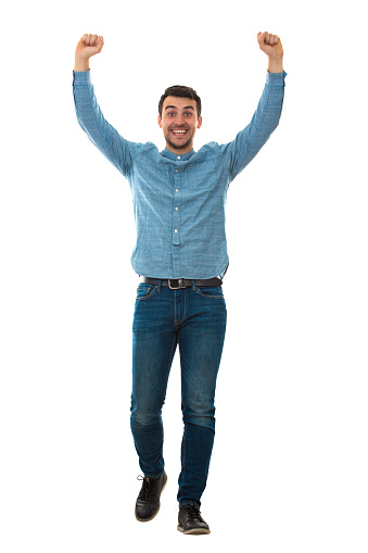 Full length portrait of a cheerfull young man raising his hands up like a winner isolated on white background.