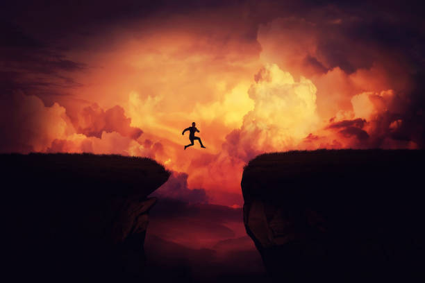 Achieving goals Fantasy self overcome concept as a businessman jump over a chasm obstacle above the clouds. Way to win and succes over sunset background. Achieving goals symbol. ravine stock pictures, royalty-free photos & images
