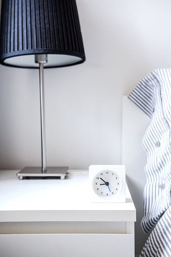 Morning alarm clock in white bedroom interior. Copyspace for text. Minimalist concept