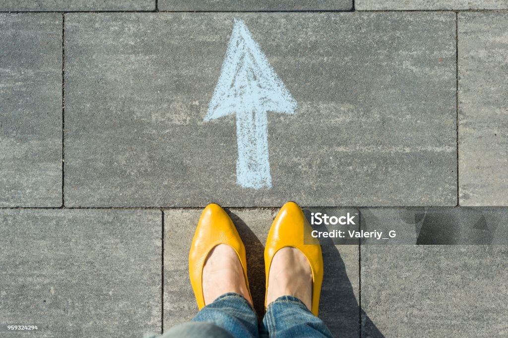 Female feet with arrow painted on the asphalt. Female feet with arrow painted on the asphalt Beginnings Stock Photo