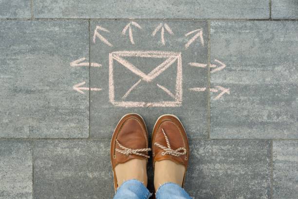 istock Female feet with abstract envelope message letter with arrows in different directions, written on grey sidewalk 959325224