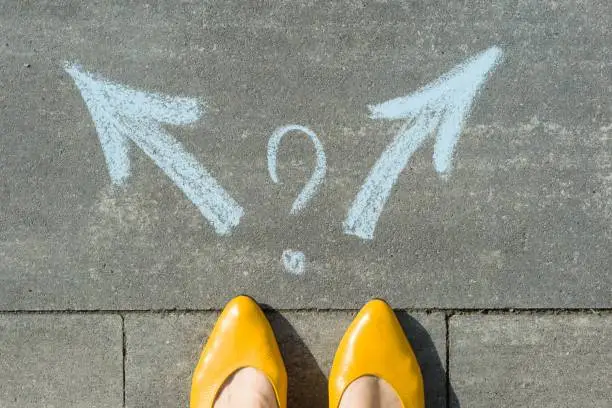 Photo of Female legs with 2 arrows and question mark, painted on the asphalt