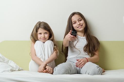 Children sitting at home in bed and watching TV. In the hands holding tv remote.