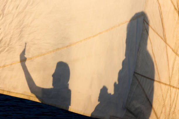 Shadow making selfie on a sail with smartphone and another shadow holding a cup