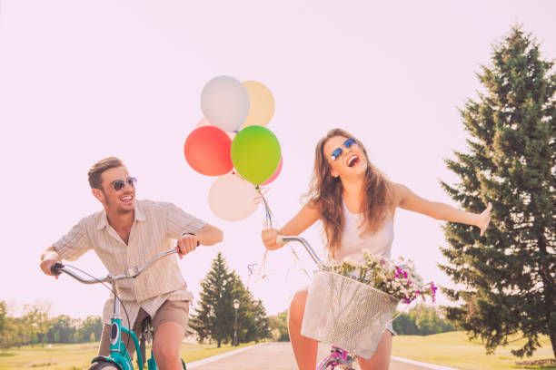 istock Cheerful happy lovers riding bikes with balloons and flowers 959352154