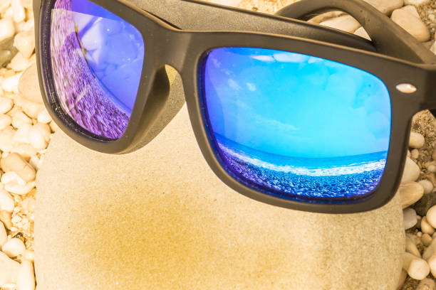 istock Blue sunglasses on a pebble beach reflecting the ocean 959352418