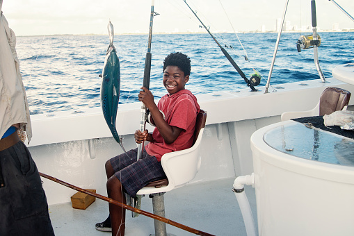 Preteen African-american boy on his first sea fishing trip on a boat. He is  proudly looking at his first catch, a beautiful bonito. Horizontal full length shot outdoors with copy space. This was taken in Florida, USA.