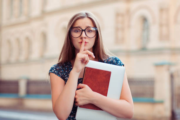 istock Shh. Student woman in glasses looking at camera keeping her forefinger by lips 959372022