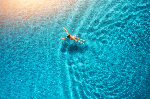 Aerial view of swimming woman at sunset in Maldives. Mediterranean sea. Aerial seascape with young girl, clear blue water, waves in summer. Transparent water. Top view. Resort on seashore. Holiday