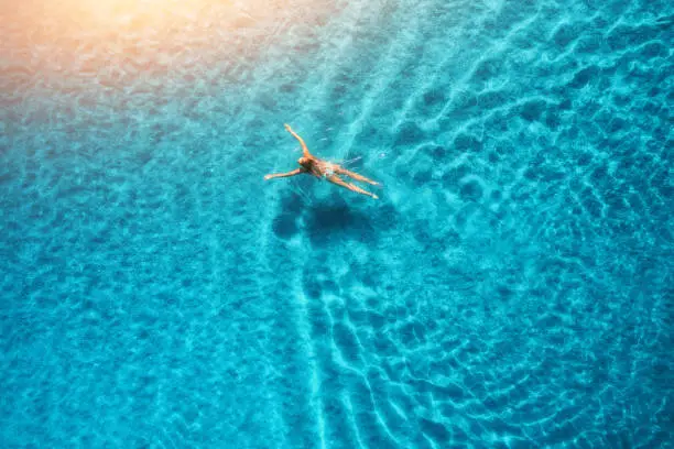 Photo of Aerial view of swimming woman at sunset in Maldives. Mediterranean sea. Aerial seascape with young girl, clear blue water, waves in summer. Transparent water. Top view. Resort on seashore. Holiday