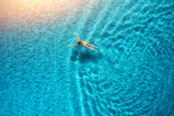 aerial view of swimming woman at sunset in maldives. mediterranean sea. aerial seascape with young girl, clear blue water, waves in summer. transparent water. top view. resort on seashore. holiday - summer people tourist slim imagens e fotografias de stock