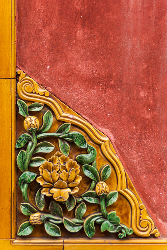 Beijing, China - April 27, 2010: Forbidden City. Closeup of flowerly corner ceramic tile decoration of a red wall shows yeillow flowers with green foliage. Lower Left corner.