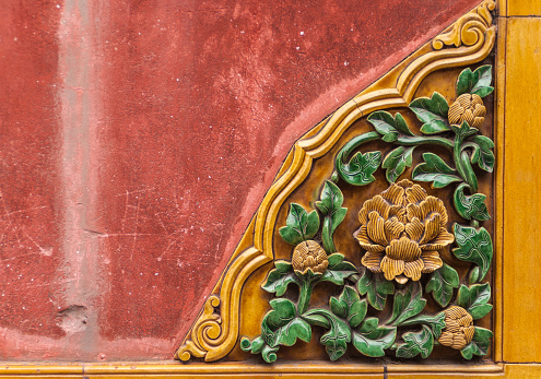 Beijing, China - April 27, 2010: Forbidden City. Closeup of flowerly corner ceramic tile decoration of a red wall shows yeillow flowers with green foliage. Lower Right corner.