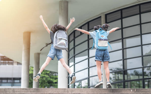 Happy school girl kids (elementary students) back view with backpacks jumping to celebrate going to class on first day of back to school education concept Happy school girl kids (elementary students) back view with backpacks jumping to celebrate going to class on first day of back to school education concept first grade classroom stock pictures, royalty-free photos & images