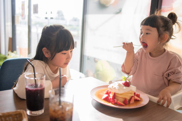 istock Little sisters eating hot cakes in cafe 959390600