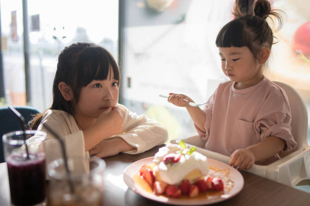 istock Little sisters eating hot cakes in cafe 959390602