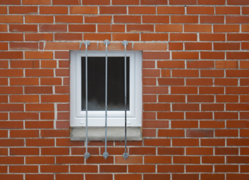 architectural detail of a barred window in a red brick wall