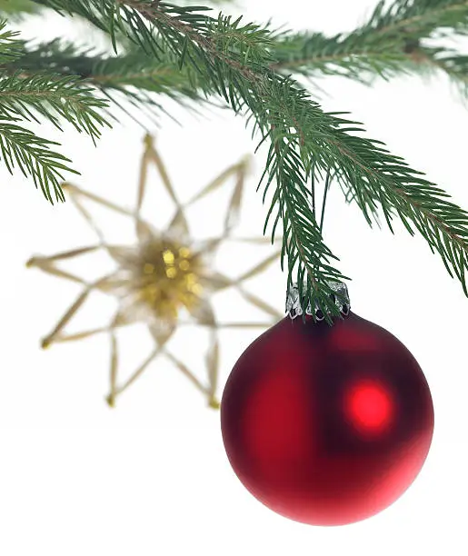 Studio photography of some christmas decoration with red christmas bauble on fir branch and a blurry straw star in the back