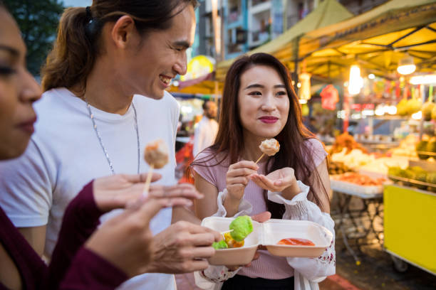 Enjoying street food at a local night market Friends eating local cuisine at a night market street food stock pictures, royalty-free photos & images