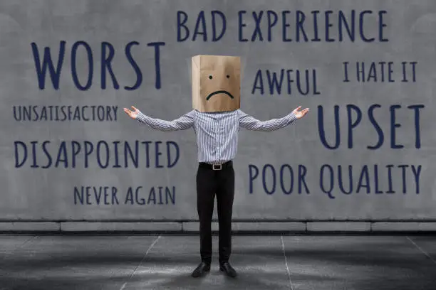 Photo of Customer Experience Concept, Unhappy Businessman Client with Sadness Emotion Face on Paper Bag, Blurred Concrete Wall with Wording of Negative Reviews as background