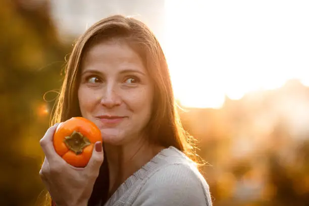 Woman eating persimmon at sunset close-up