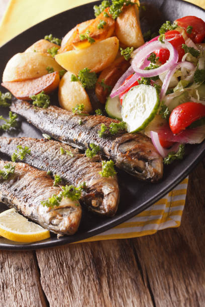 istock Fried sardines with potatoes and fresh vegetable salad close-up. Vertical 959442634