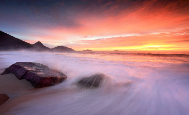 Rich red sunrise at the beach in summer Beautiful sunrise at the beach where waves washing onto the beach create splash and motion"nPort Stephens ebb and flow stock pictures, royalty-free photos & images