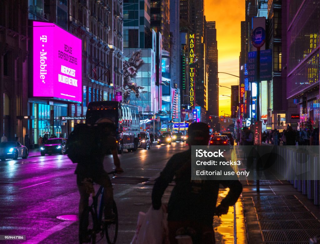 New York 42nd Street in Colorful Lights with Orange Sunset Background New York, USA - May 15, 2018: New York 42nd Street in colorful Lights with orange Sunset Background, cars, people on bicycle, glass building facades reflecting the colorful sky juxtaposed with lit up LED display panels and signages. T-Mobile Stock Photo