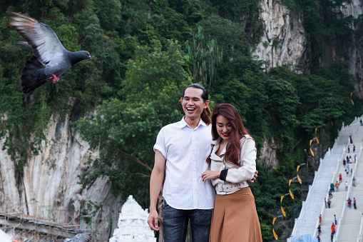 A young couple enjoy walking around near the Batu caves in Kuala Lumpur, they are watching the people feeding the doves