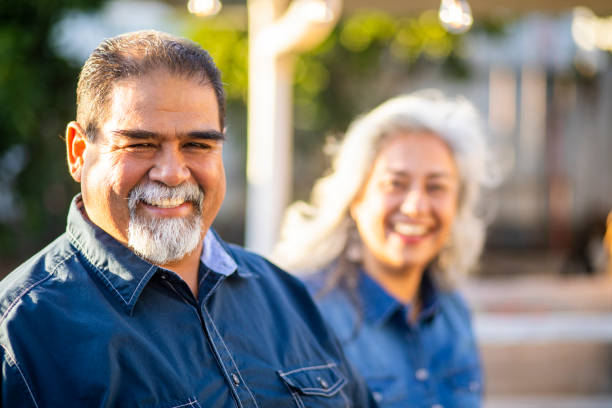 Senior Mexican Man Smiling with Wife in the Background A senior mexican man smiles at the camera with his wife in the background fat mexican man pictures stock pictures, royalty-free photos & images