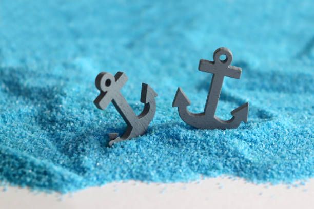 istock Two gray anchors on the blue sand. 959454896